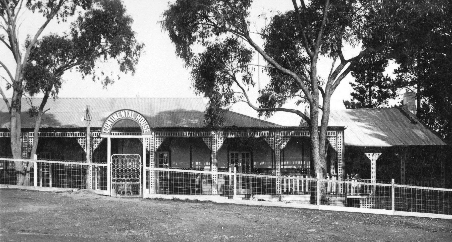 Continental House in its early years: a low verandahed building behind a picket fence, with an arched sign over the wrought-iron gate