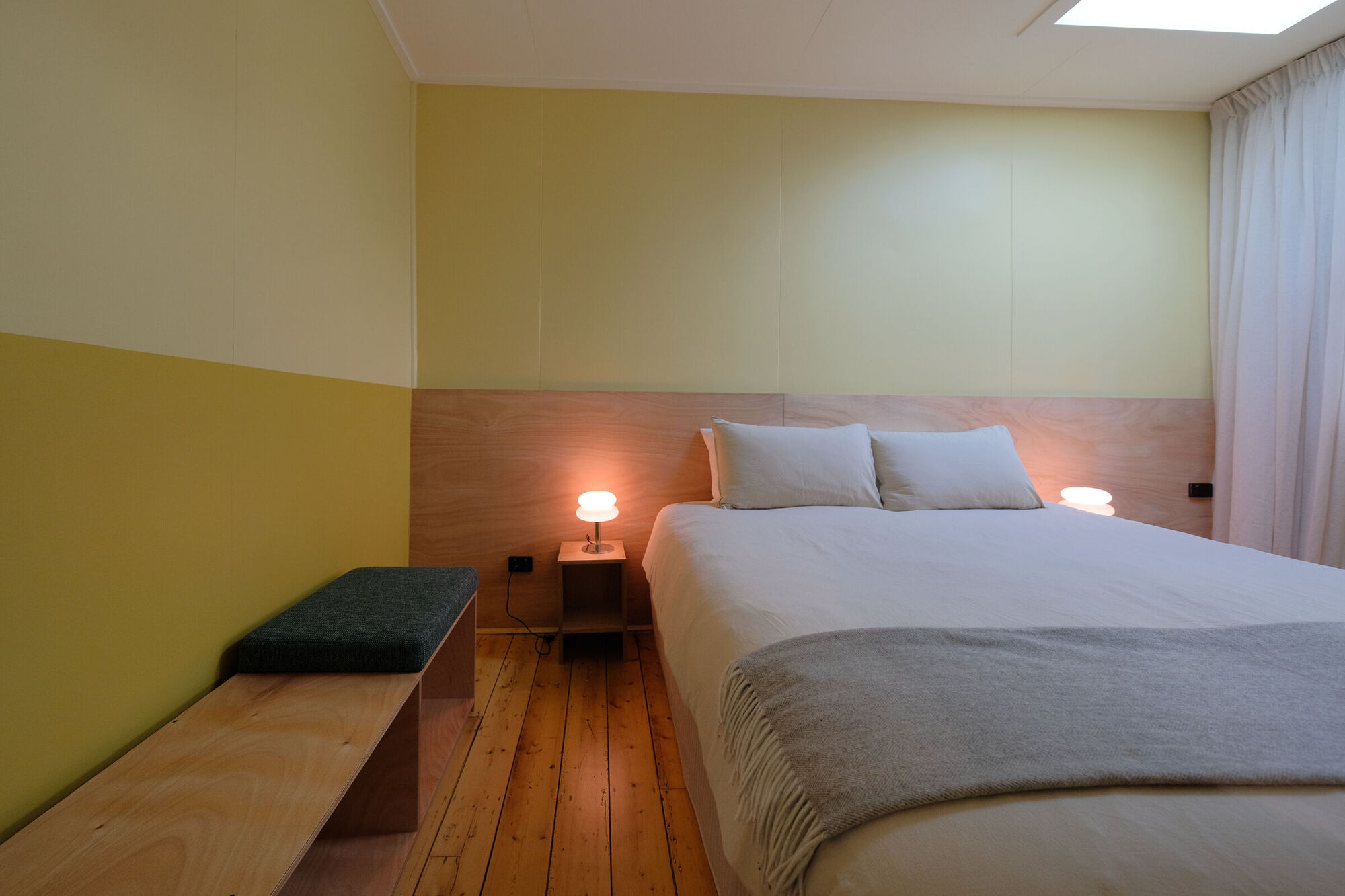 Room 7: a king bed with bedside lamps, a timber bench and soft yellow walls