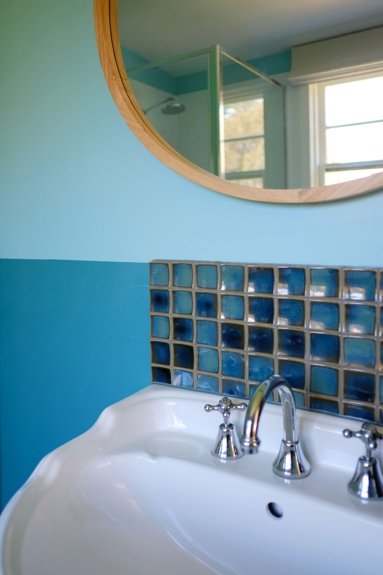 A basin with blue glass tiles and a round mirror