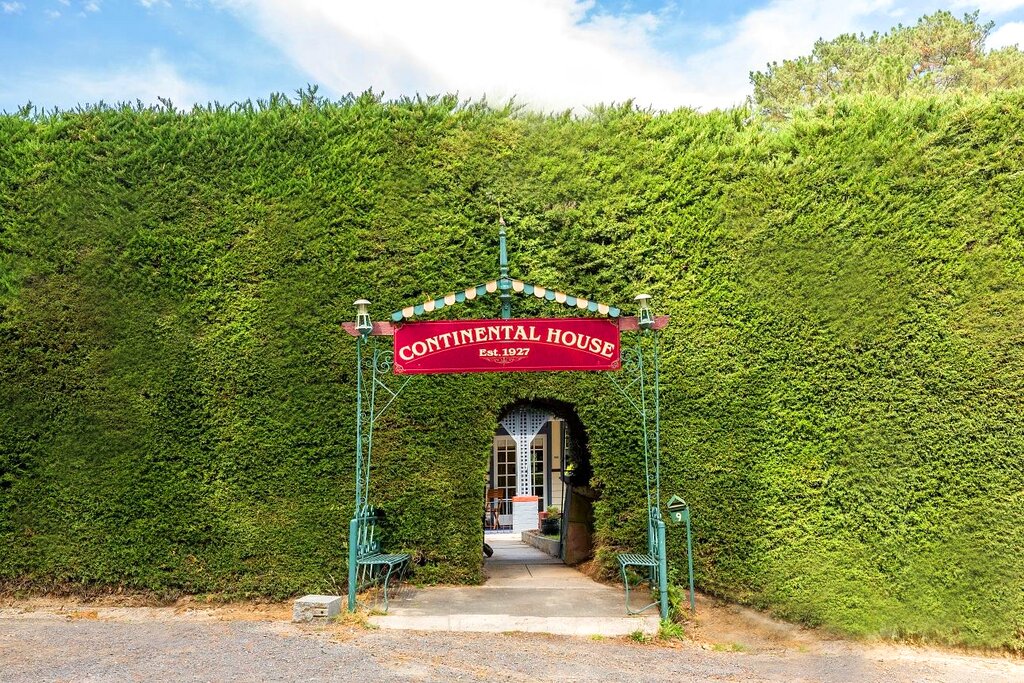 The Continental House sign above the archway cut through the tall cypress hedge
