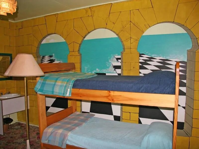 Bunk beds beneath a painted mural of arches and a chequered floor