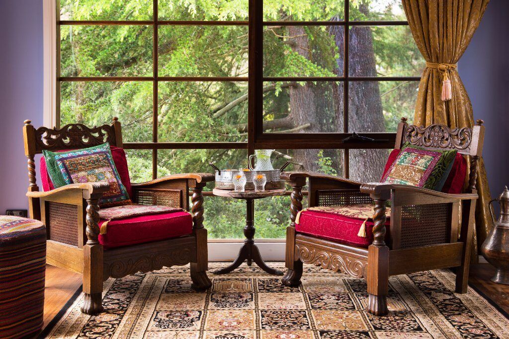 Two carved timber armchairs with red cushions by a window onto the trees