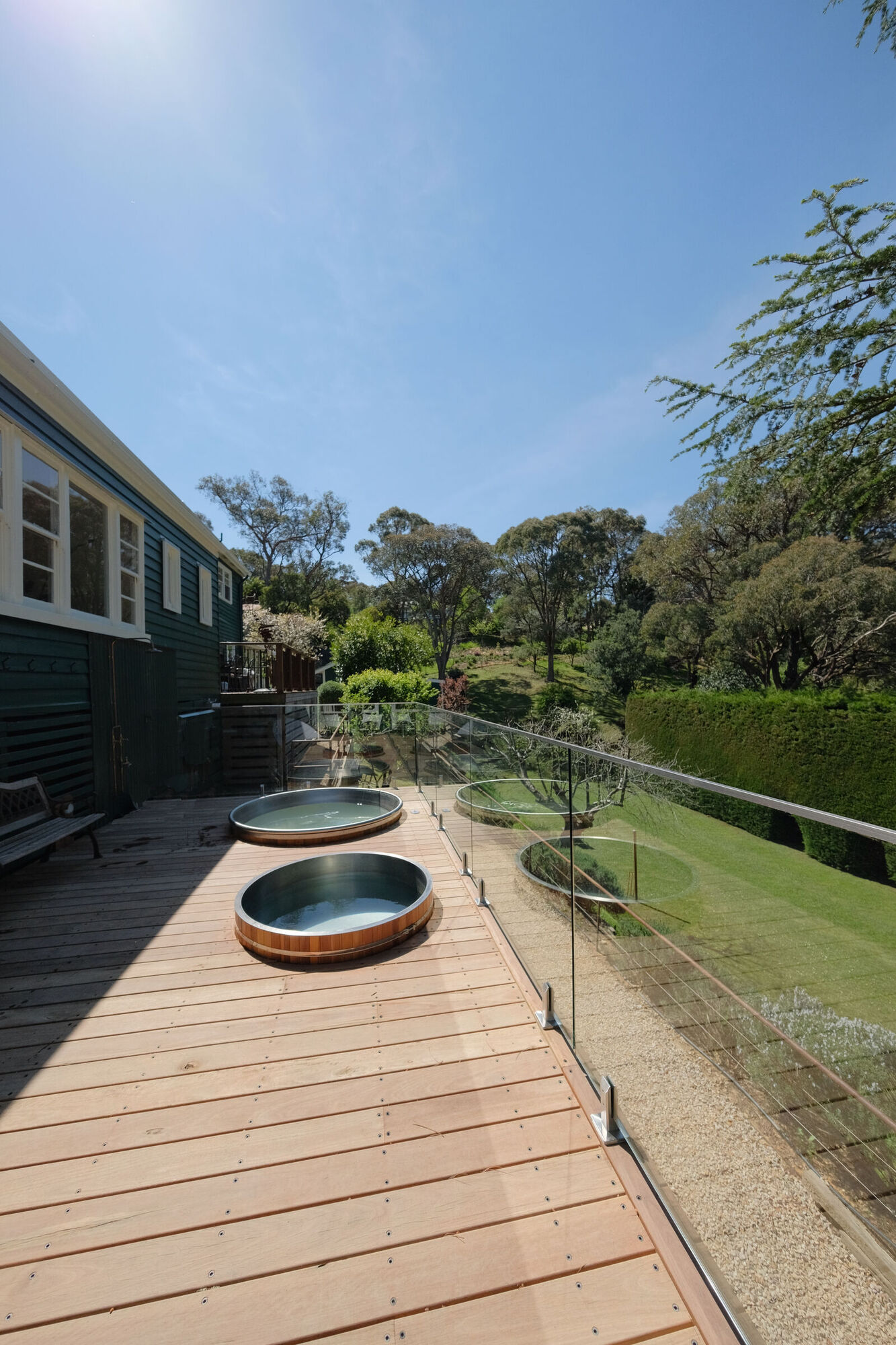 The magnesium spa and ice bath on the timber spa deck, with a glass balustrade and garden beyond